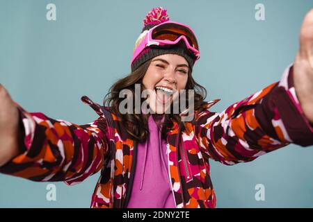 Alegre mujer joven con equipo de snowboard tomando un selfie aislado sobre azul backgorund Foto de stock