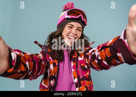 Alegre mujer joven con equipo de snowboard tomando un selfie aislado sobre azul backgorund Foto de stock