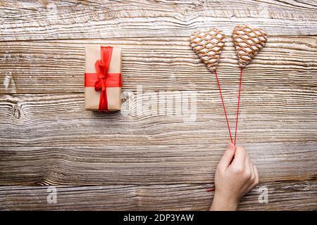 la mano sostiene dos galletas de pan de jengibre en forma de corazón en hilos rojos y una caja de regalo Foto de stock