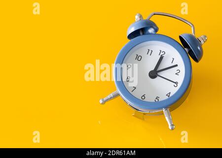 Elegante reloj despertador con cinco a doce sobre un fondo amarillo. Espacio para una inscripción a la izquierda Foto de stock