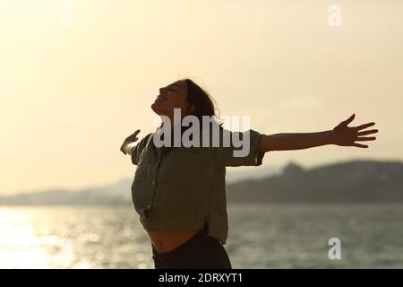 Silueta de la mujer excitado estirando los brazos de pie en la playa al atardecer