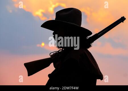 Vista lateral del hombre de Silhouette sujetando arma contra el cielo durante la puesta de sol
