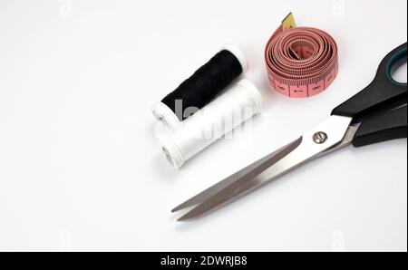 Tijeras, cinta métrica y hilos sobre un fondo blanco. Kit de costura Foto de stock