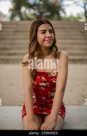 La joven con un vestido rojo está sentada en un banco. Detrás de ella hay escaleras