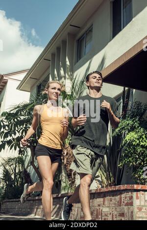 Joven hombre y mujer corriendo juntos a lo largo de la calle en el sol día Foto de stock