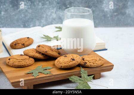 Un vaso de leche con galletas de chocolate en un tabla de corte de madera