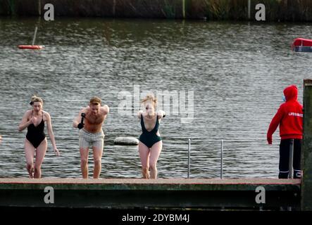 Grupo de amigos saltan a Hampstead Men's Pond para el evento anual de natación de Navidad el día de Navidad 2020 mientras lo observa un socorrista. Foto de stock