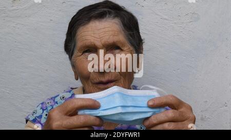 La mujer anciana tiene la máscara médica en las manos. Retrato de una mujer de 80 años arrugada sacando y doblando la máscara desechable Foto de stock