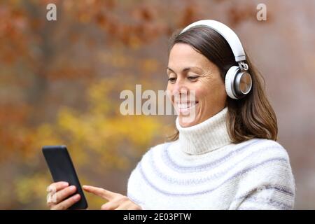 Feliz mujer adulta usando auriculares y teléfono inteligente escuchando música en un parque en otoño Foto de stock