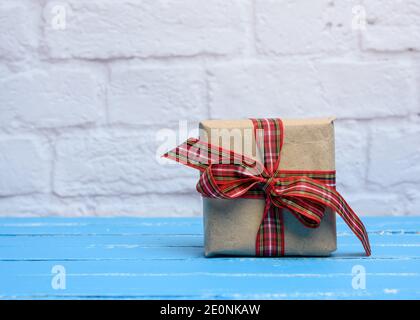 Caja de madera con regalo envuelto en papel artesanal marrón con cinta  roja, relleno de papel, vista superior desde arriba