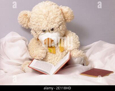 Un lindo oso de peluche beige para que los niños jueguen con él gafas está leyendo un libro Foto de stock
