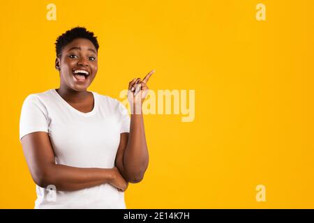 Mujer africana alegre señalando con el dedo hacia arriba teniendo idea, fondo amarillo Foto de stock