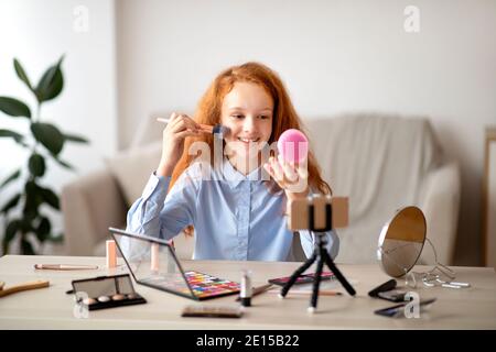 Adolescente aplicando polvo en la cara, grabando blog de belleza en el teléfono Foto de stock