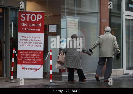 Una pareja camina pasando un cartel de consejos de coronavirus fuera de un banco en la calle Argyle en el centro de la ciudad de Glasgow la mañana después de que las medidas de bloqueo más estrictas entraron en vigor para la Escocia continental. Foto de stock