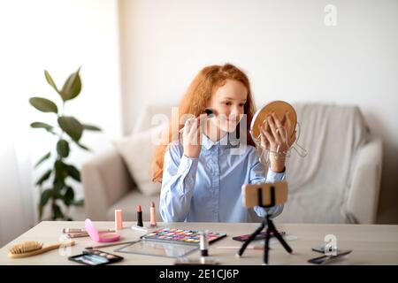 Adolescente aplicando polvo de cara, grabar blog de belleza en el smartphone Foto de stock