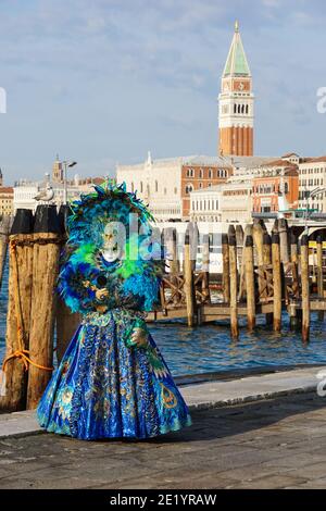 Mujer vestida con un traje tradicional decorado con plumas y máscara pintada durante el Carnaval de Venecia con el Campanile de San Marcos detrás de Venecia Italia Foto de stock