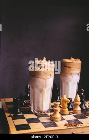 Café Dalgona. Bebida glasera batida con café instantáneo popular en Corea cóctel cremoso en copas altas decoradas con ajedrez en tablero de madera