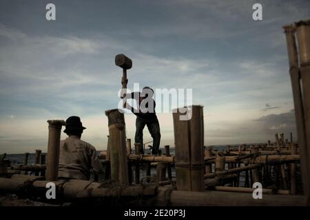 Hombres construyendo una estructura costera utilizando postes de bambú, un edificio de pilotes sobre el agua de mar en la aldea de pescadores de Cilincing, en la zona costera de Yakarta, Indonesia. Foto de archivo (2008). Foto de stock
