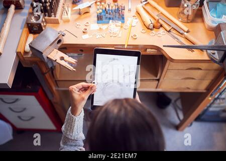 Vista aérea del joyero femenino comparando anillo con diseño dibujado En la tableta digital en Studio Foto de stock