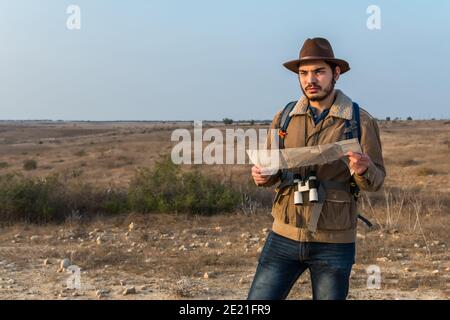 Enfoque poco profundo de un joven hiker macho de pie con binoculares y un mapa en un campo bajo la luz del sol Foto de stock