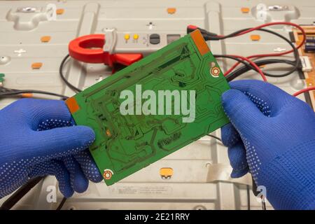 Placa de circuito verde de TV LCD en manos de un ingeniero eléctrico. Primer plano, enfoque selectivo. Foto de stock