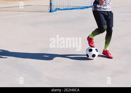 jugador de fútbol irreconocible pisando el balón en una cancha de fútbol de concreto, concepto de estilo de vida saludable y deporte urbano en la ciudad, copiar espacio