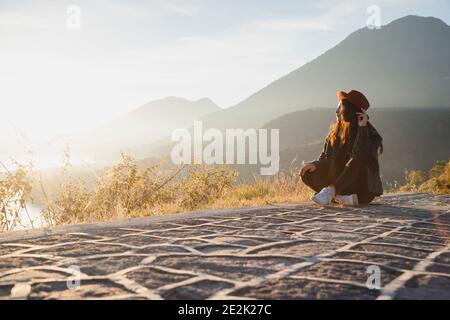 Mujer joven sentada en la cima de la montaña observando la amanecer en el Lago Atitlán - joven viajero femenino rodeado de Montañas y volcanes en Guate