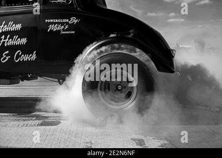 El coche de carreras de arrastre quema el caucho de su neumático con mucho de humo de los neumáticos quemados en la pista de velocidad Foto de stock