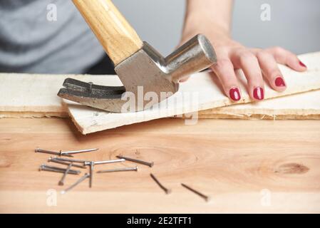 Detalle de la carpintería, una joven mujer caucásica con sus uñas hecho quitar un clavo de un pedazo de madera usando un martillo de garras Foto de stock