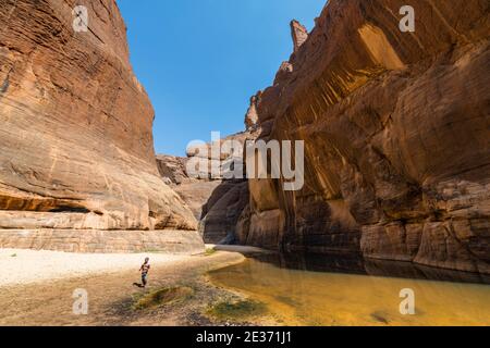 Niño en el pozo de agua de Guelta d'Archei, garganta de roca, meseta Ennedi, Chad Foto de stock