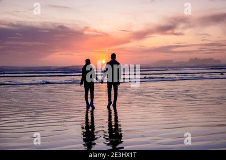 Pareja de hombres y mujeres de mediana edad viendo la puesta de sol en la playa de Tofino Vancouver Island Canadá, hermosa puesta de sol en la playa con colores rosa-púrpura en el cielo. Canadá Tofino