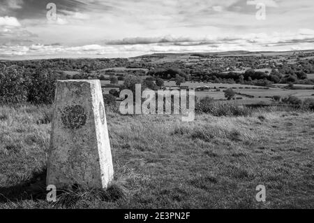Alrededor del Reino Unido - Trig Point en la colina de Hough, Chorley, con vistas hacia Darwen Moors & Darwen Tower capturado en blanco y negro Foto de stock