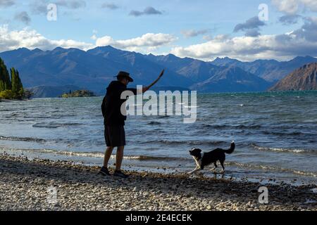 Tiro de un joven con sudaderas con capucha y de pie en la orilla del lago Wanaka con un icónico árbol solitario. Isla Sur de Nueva Zelanda.