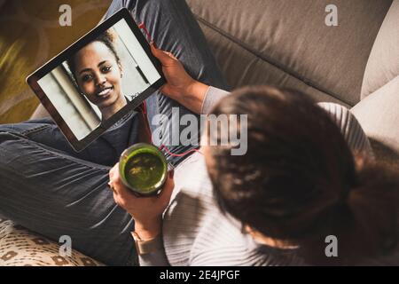 Mujer madura teniendo smoothie mientras que hace chat de vídeo en casa