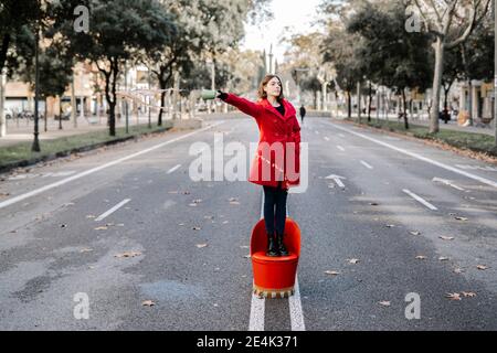 La mujer joven tiene las manos en los bolsillos derramando café mientras está de pie silla en la carretera