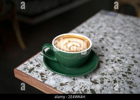 Taza de café blanco plano en una taza verde con hermoso arte latte, sobre mesa de mármol.