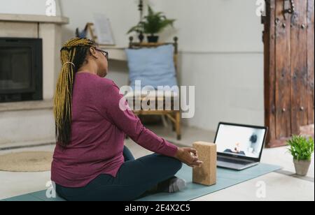 Mujer africana de edad avanzada haciendo yoga virtual de la clase de fitness con portátil En casa - e-learning y bienestar de la gente concepto de estilo de vida Foto de stock