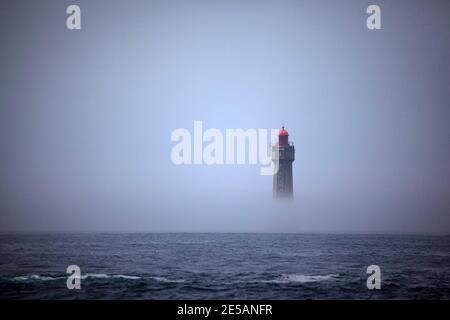 El espectacular faro de la Jument, rodeado de niebla de verano, frente a la costa de la Ile d'Ouessant, Bretaña. El icónico faro de 47 metros de altura era bui