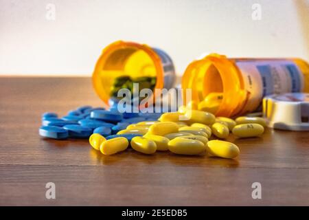 Dos botellas de prescripción volcó con amarillo y azul píldoras derramándose sobre la mesa. Las píldoras son enfocados con las botellas fuera de foco. Foto de stock