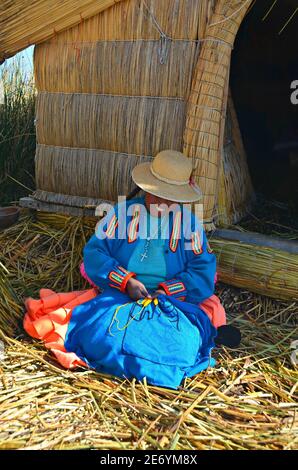 Mujer indígena Uru frente a su casa de juncos en una isla flotante autoformada, haciendo artesanías en el Lago Titicaca, Puno Perú. Foto de stock