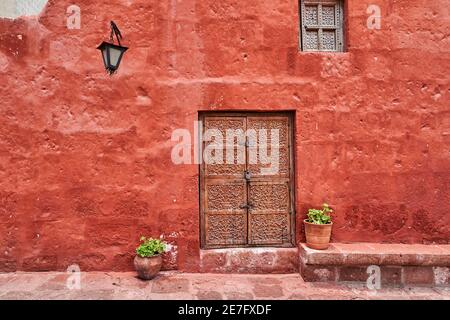 edificio colonial español de color rojo intenso en la fachada, una linterna y una antigua puerta de madera con adornos Foto de stock