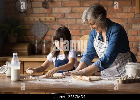 Cierra a la abuela feliz con la nieta rodando la masa Foto de stock