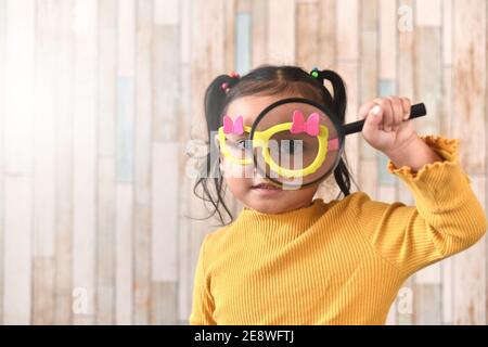 Linda niña asiática mirando a través de una lupa. Concepto de curiosidad aprendizaje infantil y visión