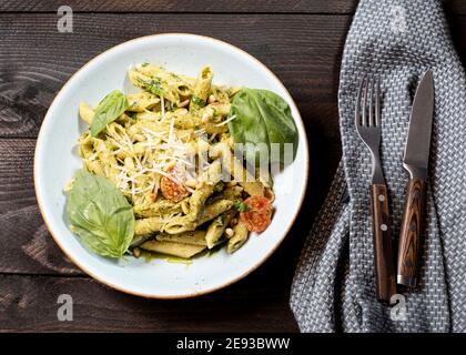 Pasta Rigatoni con pesto y piñones sobre un marrón mesa de madera con cuchillo y tenedor Foto de stock