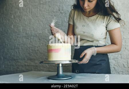 Una cocinera de pastelería hace un pastel de boda con sus propias manos y aprieta la crema en las capas del pastel. Un chef de pastelería hace una crema rosa utilizando un Foto de stock