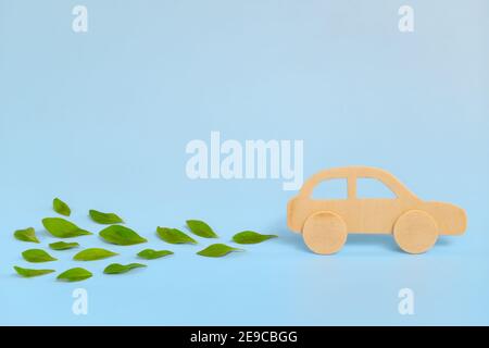 Modelo de coche de madera que emite hojas verdes frescas sobre fondo azul. Energía sostenible, limpia y verde y biocombustible y biodiesel para el transporte