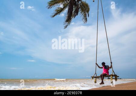 Mujer africana sentada junto al mar en una silla colgante. Axim Ghana West Africa Beach 2018 2 de noviembre