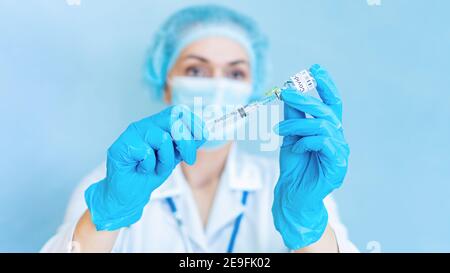 Vacunación contra el coronavirus. Pruebas de las vacunas COVID-19. Una doctora en una máscara médica llena una jeringa con una vacuna COVID-19 en una ba azul Foto de stock