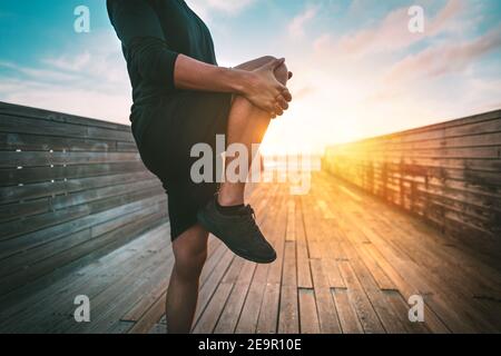 Hombre de fitness calentándose y estirando las piernas antes de entrenar al aire libre al atardecer o al amanecer. Deporte y estilo de vida saludable