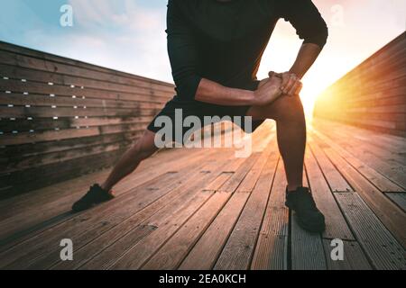 Hombre estirando los músculos aductores de la pierna y calentándose para entrenar al aire libre